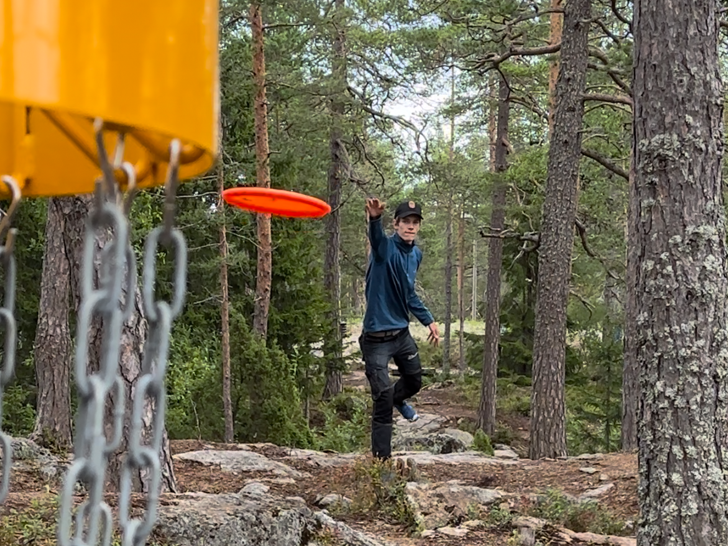 Bilden visar en discgolfspelare som kastar emot en korg på Södra Berget i Sundsvall.